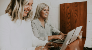 a couple of women sitting at a desk using a laptop