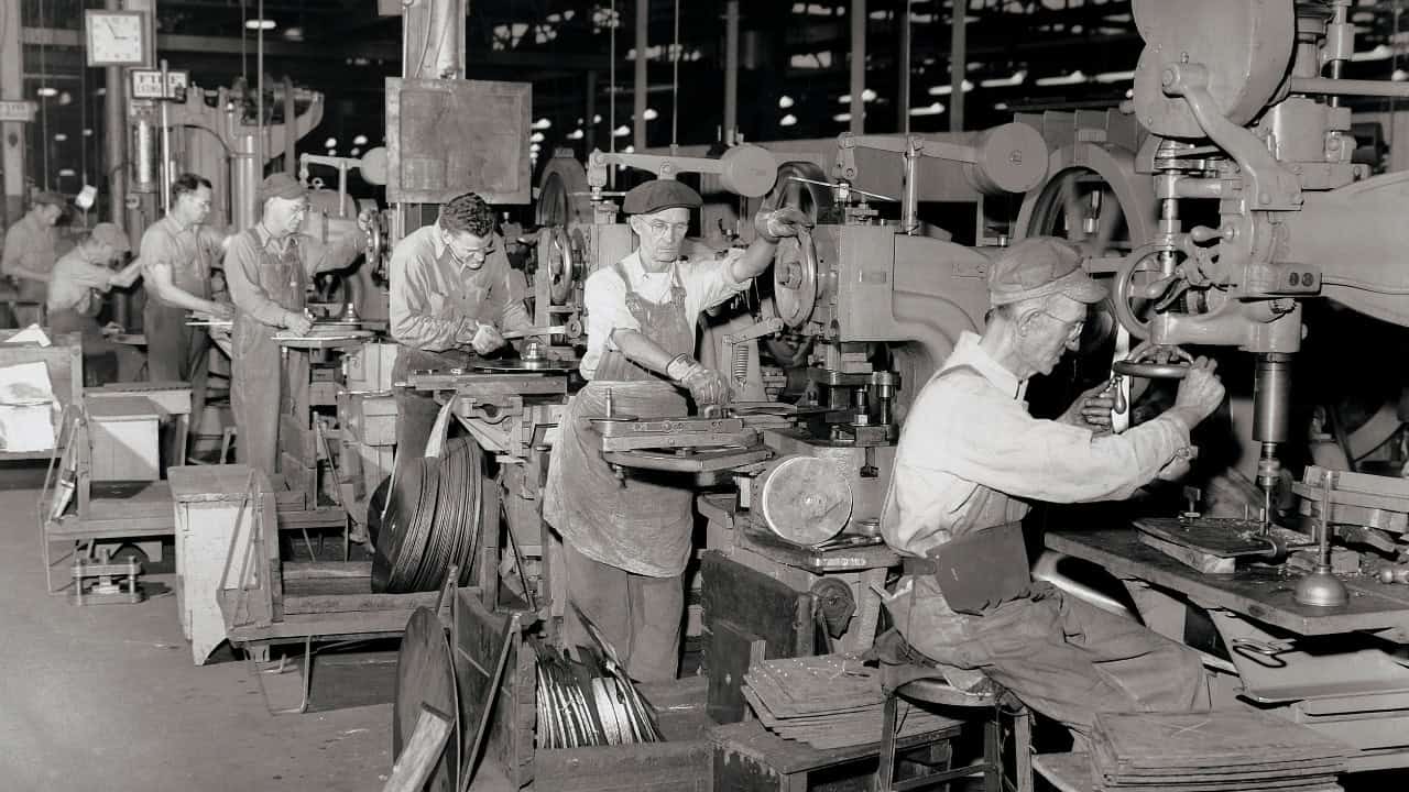 L&D of the 20th century, demonstrated by a line of older men working in a factory.